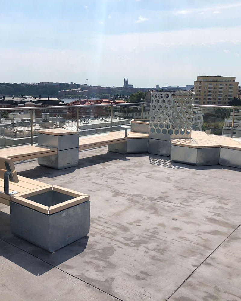 A shot overlooking a city, the patio area has casual modular seating combination of bechnes and planters on the rooftop of a building.